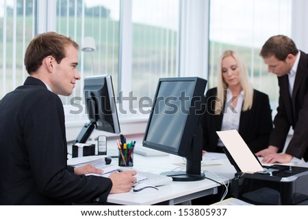 Dedicated businessman working at his desk in the office taking notes from information on the computer monitor