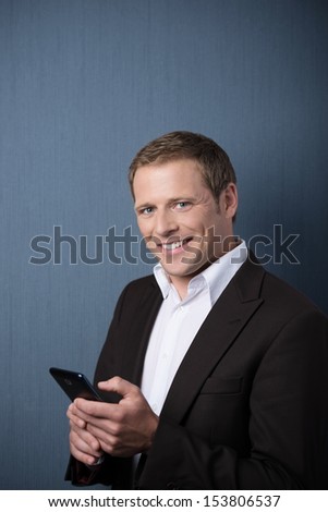 Smiling handsome young business man with a mobile phone in his hands standing looking sideways at the camera against a blue background