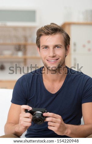 Handsome young man with a small compact digital camera in his hands giving the viewer a friendly relaxed smile