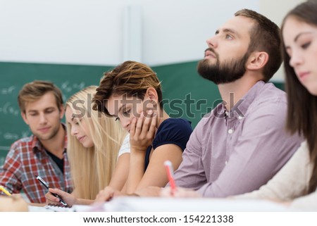 Young thoughtful male university student sitting in a group of students busy studying at a table with his head tilted back as he tries to solve a problem or seek inspiration