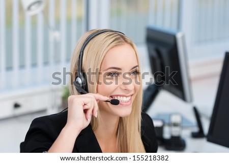 Friendly attractive young female call centre operator or receptionist wearing a headset and listening to the conversation with a lovely wide smile