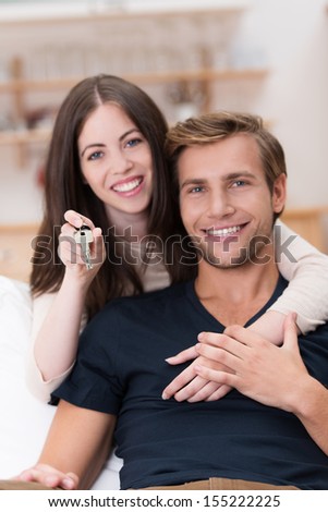 Happy affectionate young couple in an affectionate embrace looking at the camera with cheerful grins as they relax at home