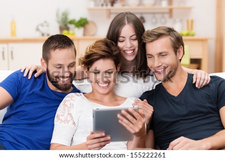Group of happy young men and women sitting on a sofa together sharing a tablet computer and reading information on the screen