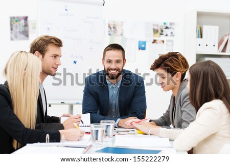 Group of business people in a meeting seated grouped around a table having a discussion with focus to a smiling man at the head of the table