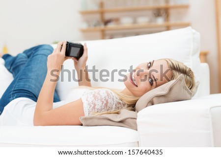 Beautiful blond woman with a camera lying relaxing on her back on a sofa turning her head to look back at the viewer with a beaming smile