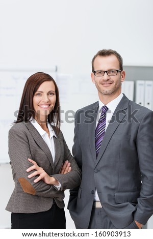 Stylish confident business team with an attractive man and woman standing side by side in the office looking at the camera with friendly smiles