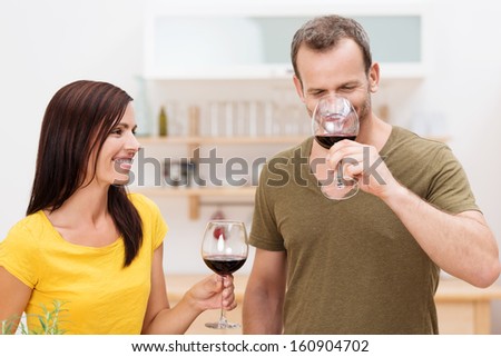 Smiling attractive young couple enjoying a glass of red wine in the kitchen standing relaxing at home