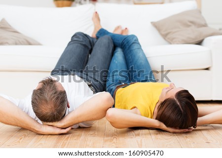 Young couple sharing a relaxing day lying side by side on their backs on a wooden living room floor with their bare feet up on the sofa