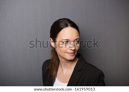 Thoughtful attractive businesswoman pausing to look back over her shoulder with a smile, head and shoulders portrait on grey