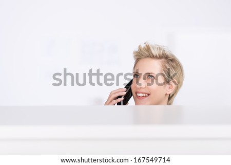 Happy woman working behind a counter with just her head visible as she chats on a phone with a smile of delight