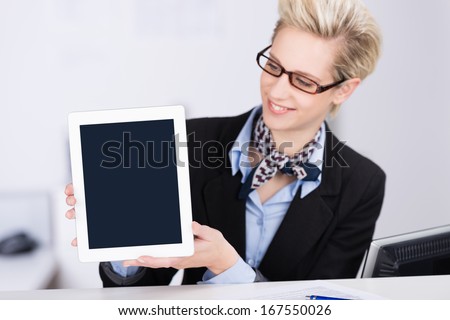 Efficient stylish receptionist wearing glasses with a modern blond hairstyle displaying a tablet computer with the blank screen towards the camera