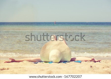 View from the top of her head of a woman lying sunbathing on a beach wearing a straw sunhat with a wide rim, low angle view towards the sea