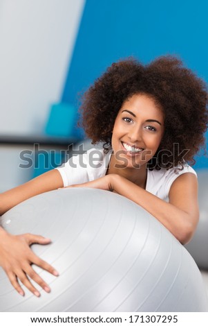 Happy young African American woman with a wild afro hairstyle in a gym with a pilates ball looking at the camera with a beaming vivacious smile
