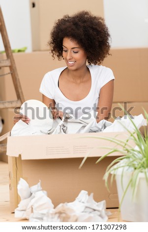Attractive young African American woman unpacking cartons in her new house kneeling on the floor surrounded by crumpled white packing paper