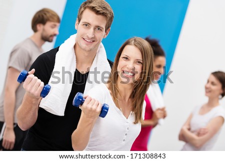Enthusiastic young couple working out with dumbbells at the gym looking at the camera with beaming smiles in a health and fitness concept
