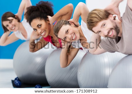 Diverse group of young friends having fun at the gym working out with gym balls doing Pilates exercises to tone their muscles turning to smile at the camera