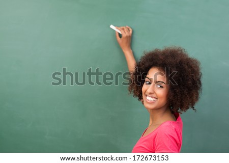 Beautiful African American student or teacher standing in front of the blank class blackboard with a piece of chalk in her hand ready to commence writing
