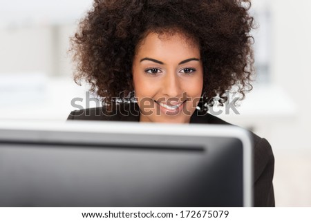 African American businesswoman at work sitting at her desk reading information on her computer monitor