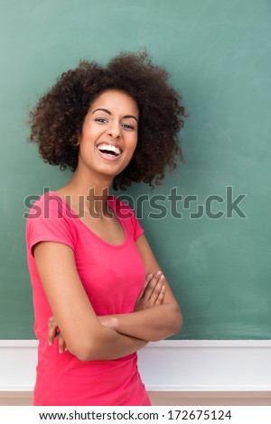 Laughing African American woman with a frizzy afro hairstyle and a joyful sense of humor standing smiling at the camera with folded arms