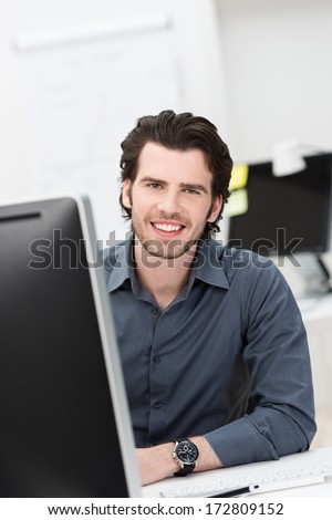 Successful confident businessman with a warm friendly smile sitting at his desk in the office looking at the camera