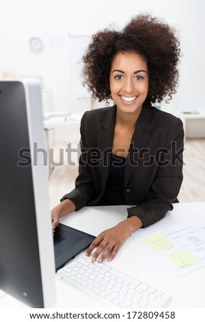 Happy African American businesswoman sitting working at her desktop computer looking at the camera with a beautiful smile