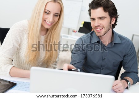Two friends or partners working together in the office as they sit in front of a computer discussing a project or planning a business strategy