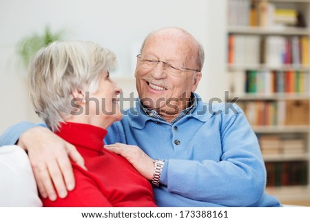 Romantic senior couple relaxing at home sitting on a sofa looking into each others eyes with focus to the mans face which has the most beautiful loving tender smile