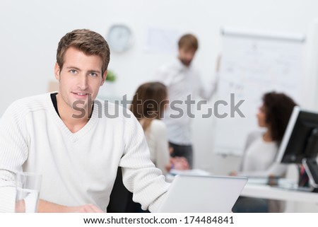 Handsome businessman working in a busy office sitting looking at the camera with a friendly smile
