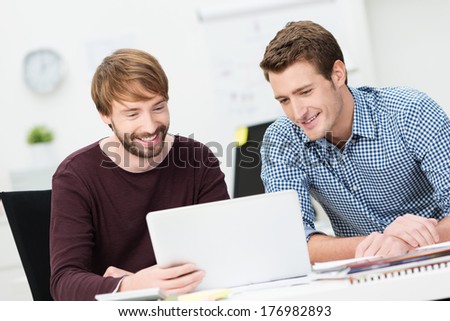 Two happy businessmen working together in the office sharing a laptop computer as they discuss a project