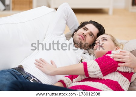 Young couple relax in each others arms on a sofa lying on their backs staring dreamily up into the air
