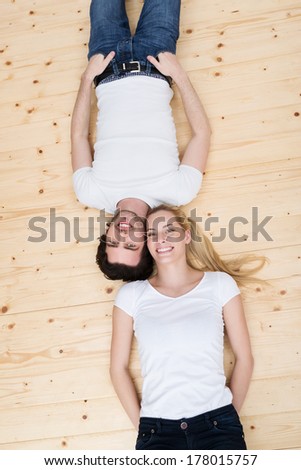 Happy attractive young couple relaxing on the floor lying head to head on their backs smiling up at the camera