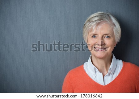 Attractive grey-haired senior woman with a beaming smile posing against a dark grey background with copyspace and vignetting