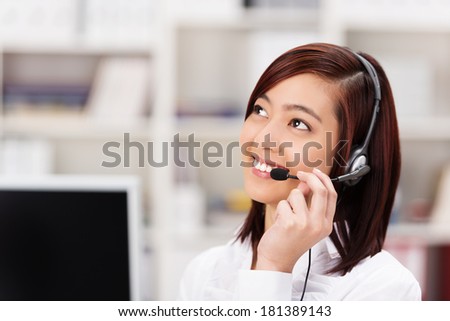 Friendly young Asian call centre operator chatting on the headset phone and smiling as she listens to the customer speaking as she tries to assist