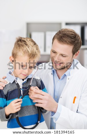 Cute young boy listening to his heartbeat with a stethoscope as the friendly male pediatrician puts him at his ease during a consultation at the hospital