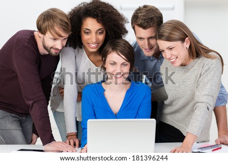 Excited young business team grouped together looking at a laptop as they review their latest presentation together smiling in satisfaction