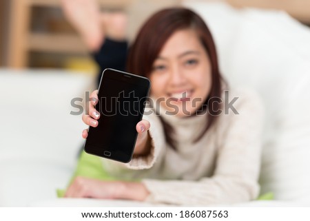 Young smiling Asian woman holding up her mobile phone with the blank black screen facing the camera drawing your attention to the copyspace