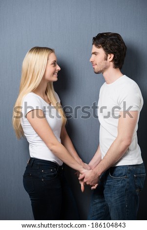 Loving couple standing holding hands facing one another smiling into each others eyes as they share a tender moment