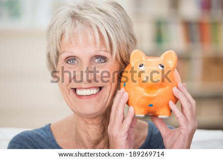 Excited senior woman holding up her piggy bank smiling in anticipation of a planned vacation or purchase to be paid for from her nest egg and savings