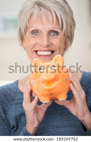 Smiling elderly woman holding a piggy bank in her hands as she enjoys her retirement thanks to her nest egg and savings, focus to her face