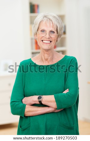 Relaxed confident beautiful senior woman standing wearing her reading glasses with folded arms and a lovely warm friendly smile
