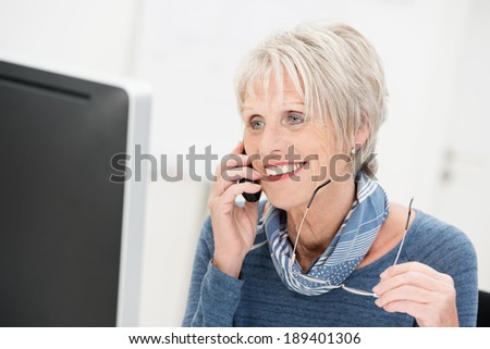 Attractive senior businesswoman chatting on the phone smiling as she listens to the call while holding her glasses in her hand