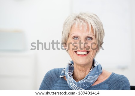 Trendy attractive senior woman with a lovely charming smile wearing a stylish scarf, head and shoulders portrait with copyspace