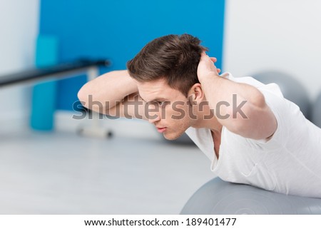 Fit young man working out doing pilates exercises with his hands clasped behind his head concentrating as he tones and strengthens his muscles