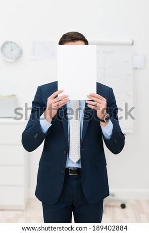 Elegant Businessman in a stylish suit hiding his face behind a blank white sheet of paper with copyspace for your text