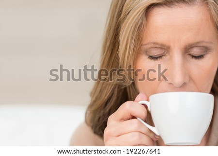 Attractive middle-aged woman savouring a fresh cup of coffee as she smells the aroma with a look of appreciation and downcast eyes