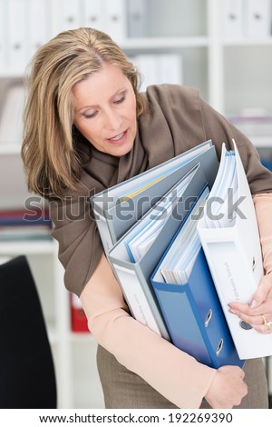 Frustrated attractive middle-aged businesswoman struggling with an armful of office files as they fall all over the place a she tries to move them