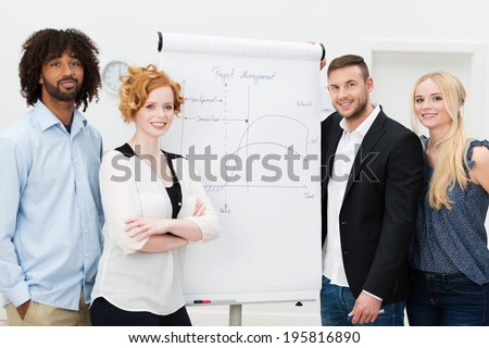 Happy successful business people standing grouped around a flip chart during an in house training session and presentation, men and women present