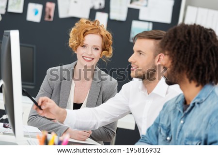 Creative multiethnic young business team at work in the office sitting in front of a large desktop monitor discussing a design initiative