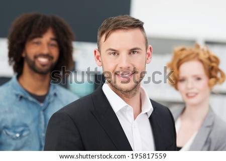 Smiling young business manager posing with members of his team standing behind him looking directly at the camera