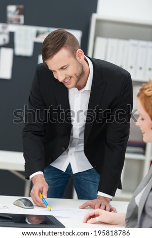 Businessman standing chatting with a female co-worker smiling as they discuss paperwork spread out on her desk